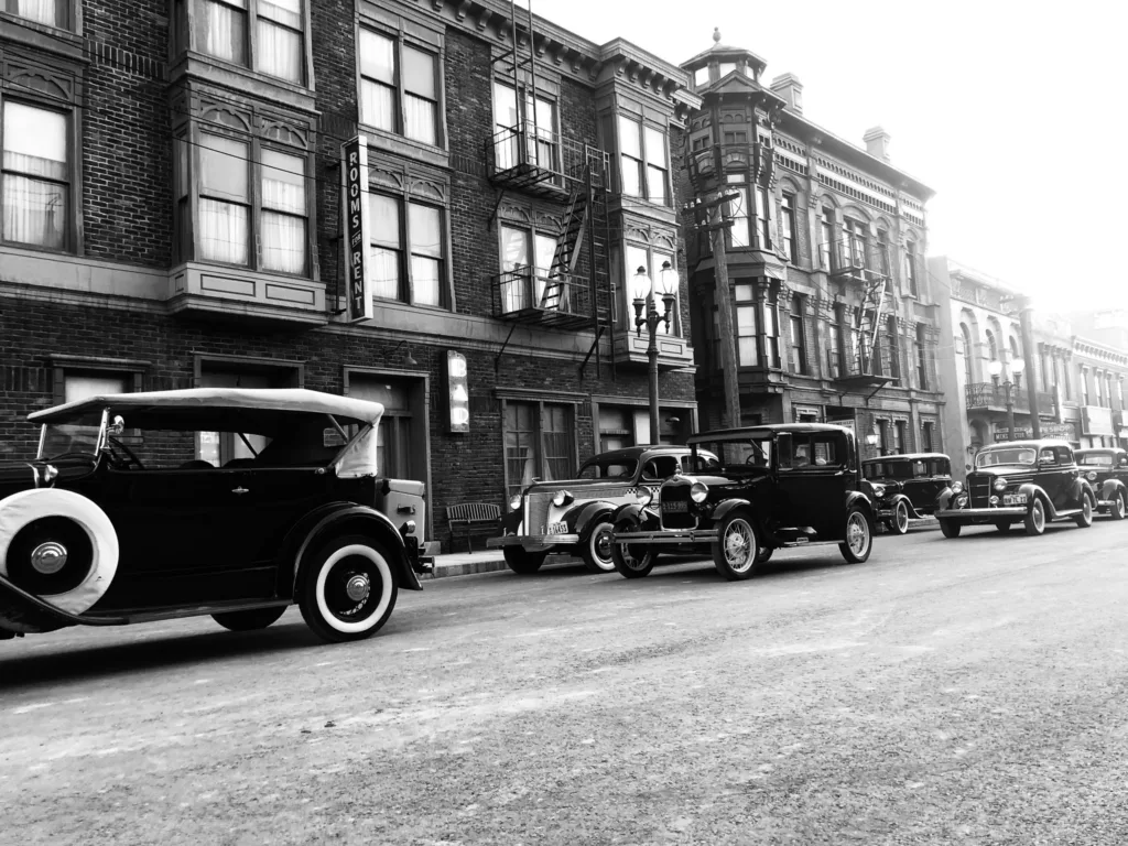 A black and white photo of old cars parked in front of a building.